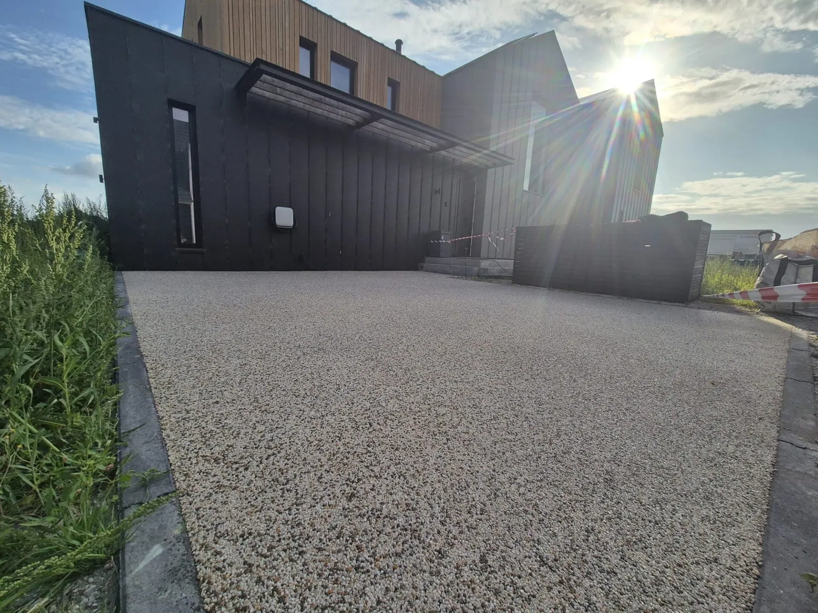 Lichtgrijze oprit van harsgebonden grind voor een moderne woning met donkere gevel