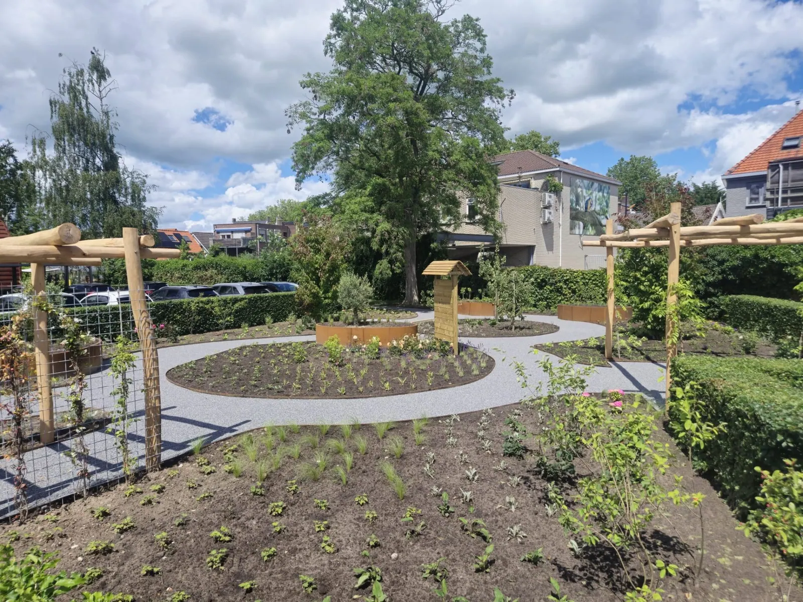 Grote tuin in parkstijl met een rond pad van licht harsgebonden grind en houten pergola's