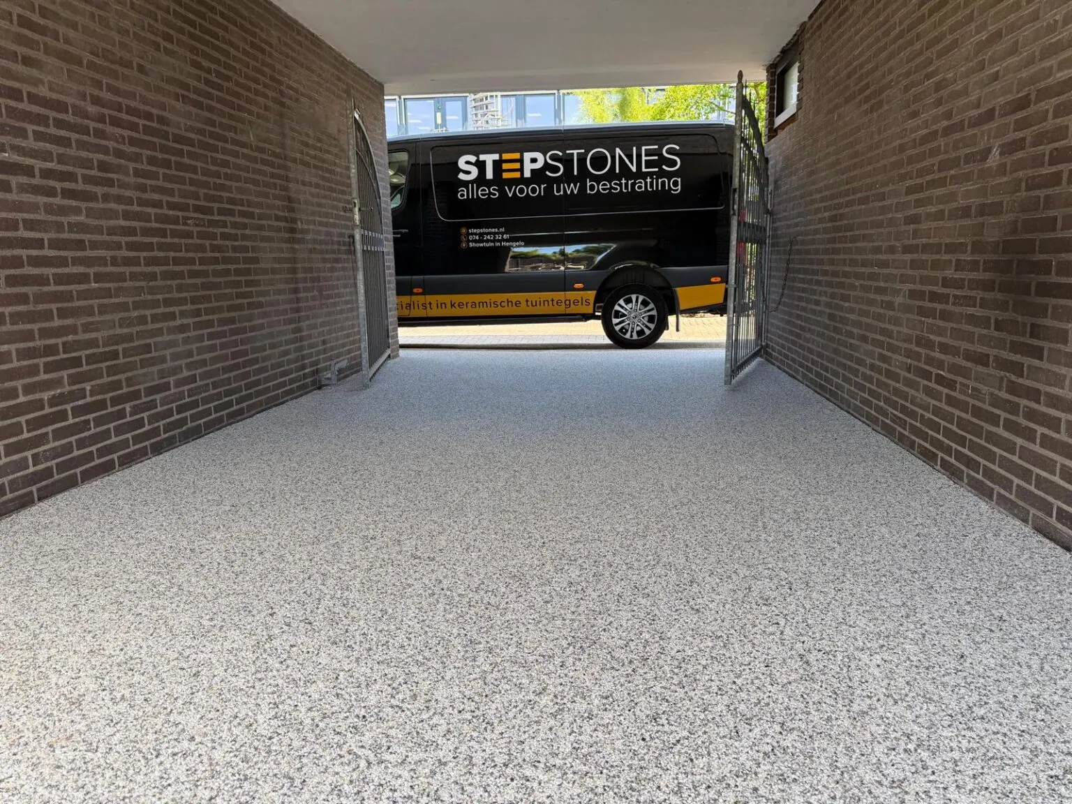 Carport met een lichte vloer van harsgebonden grind tussen twee bakstenen muren