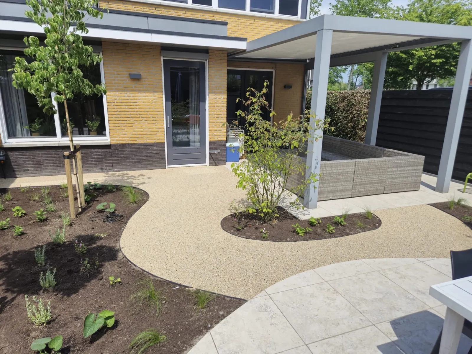 Licht beige pad met vloeiende bocht in de voortuin bij een woning met pergola