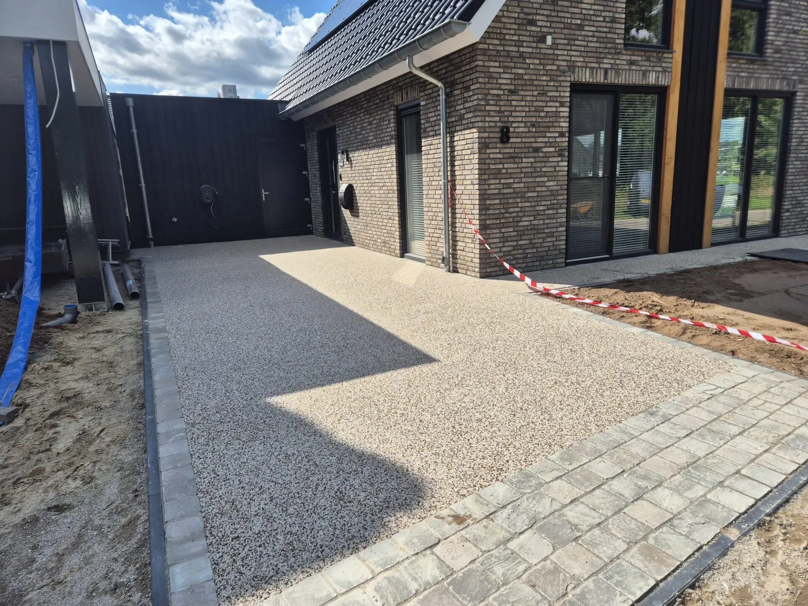 Net aangelegde strook harsgebonden grind met een klinkerrand, naast het zandbed van de tuin.