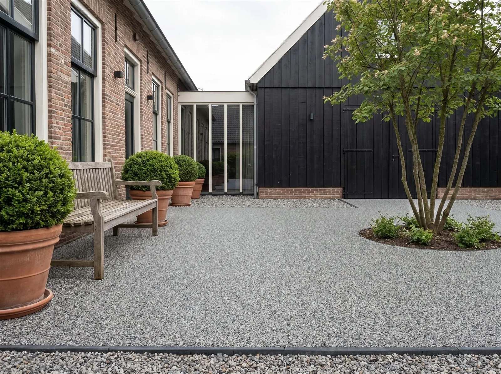 Sfeerimpressie: een binnenplaats tussen woonboerderij en schuur met harsgebonden grind in Solid Grey