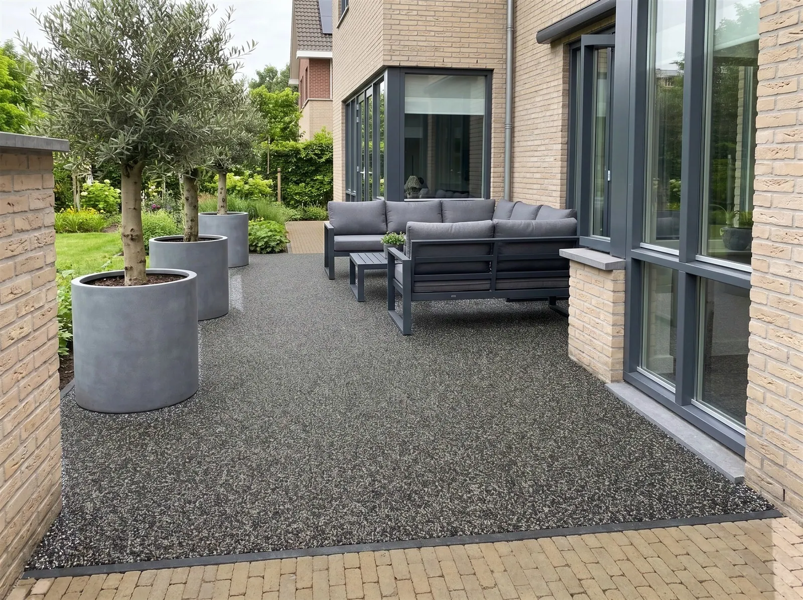 Sfeerimpressie: een modern loungeterras met olijfbomen in grijze bakken, met een grindtapijt van harsgebonden grind in Mystic Grey